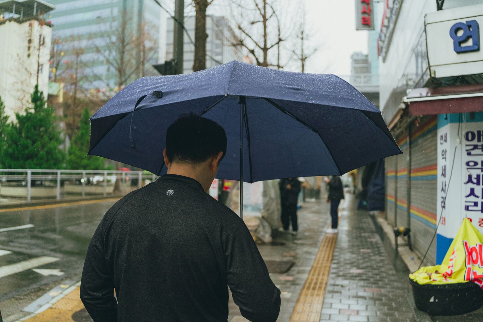 首尔雨中,一个人撑着深色伞走在湿街上